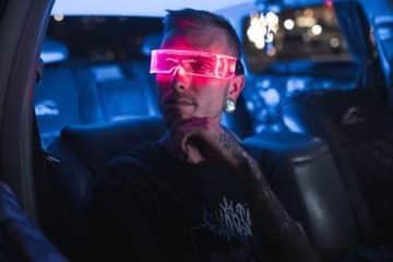 A young man with LED sunglasses sits in a car, creating a sci-fi vibe.