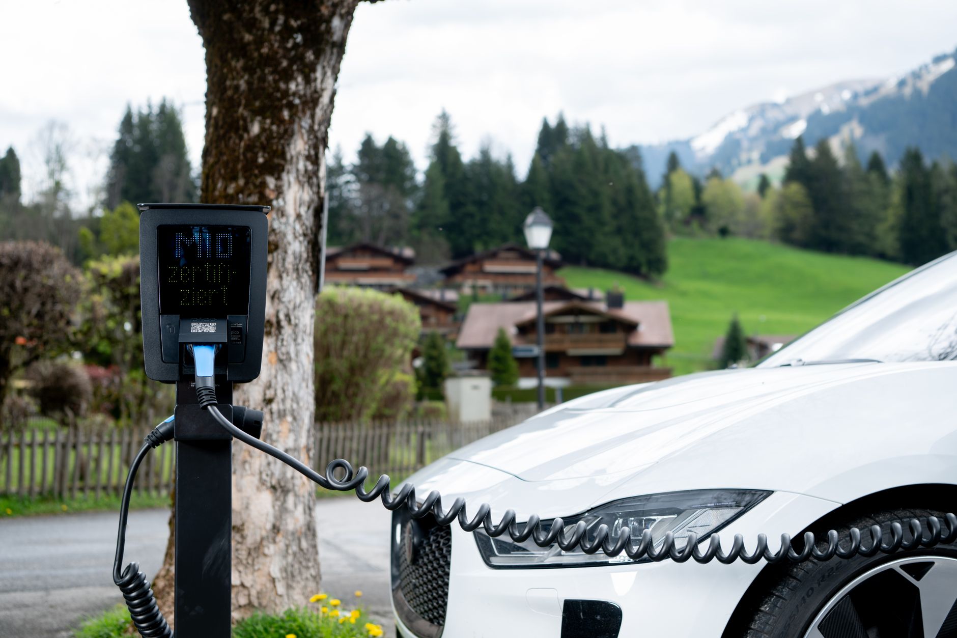Voiture blanche reliée à une borne de recharge électrique