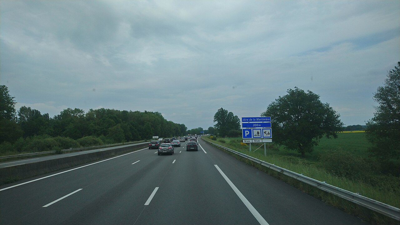 Autoroute A11 avec quelques véhicules au loin et un panneau annonçant une aire de repos.