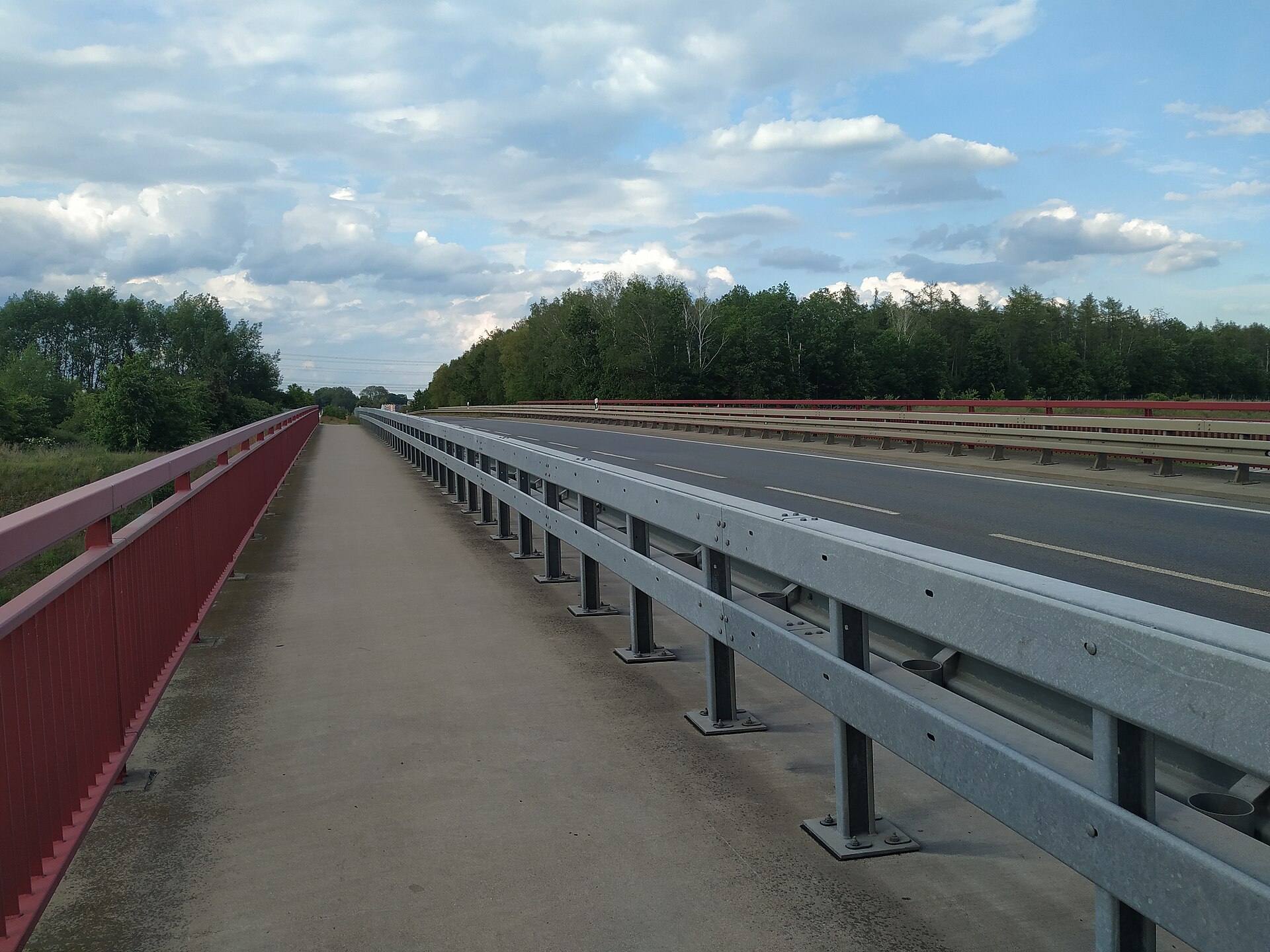 Un pont au-dessus d'une autoroute déserte, bordée de glissières et de forêt